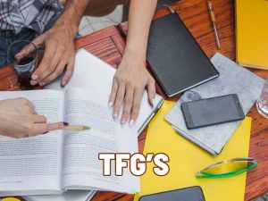 Manos de estudiantes revisando notas y material de estudio para un TFG en una mesa.