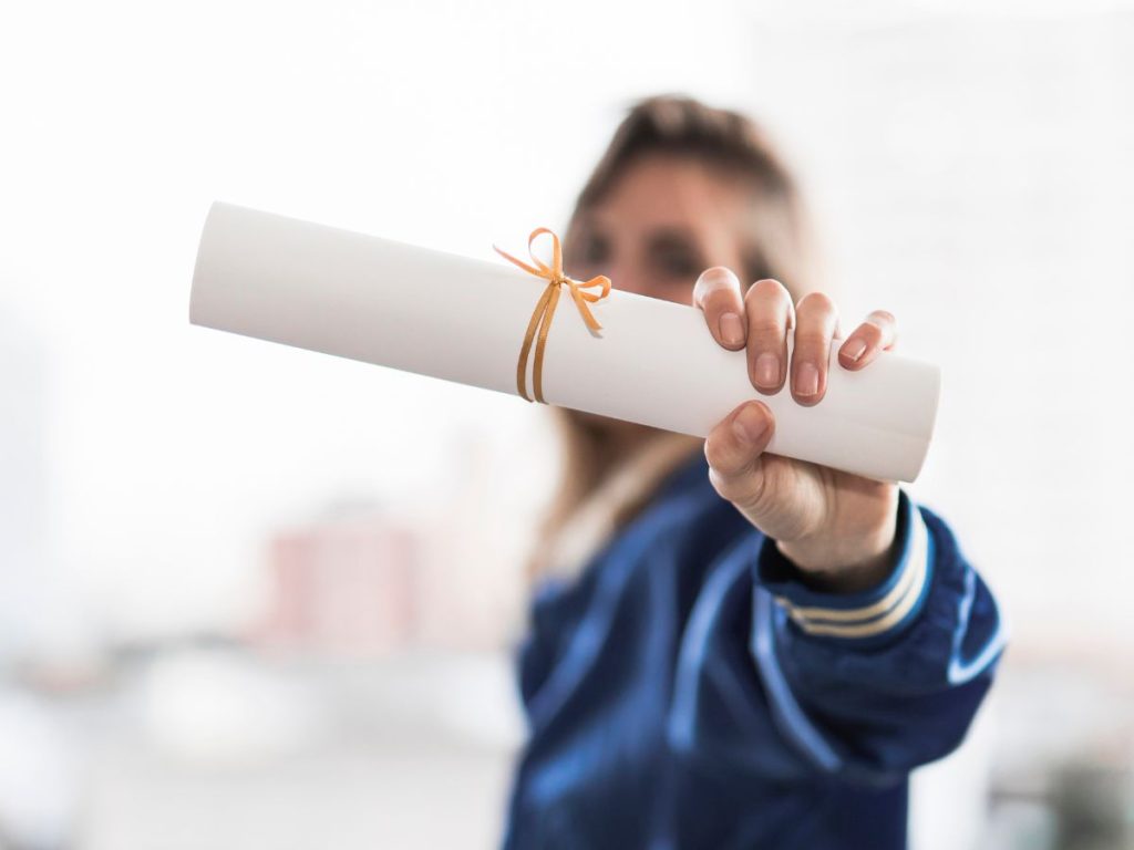 Chica de fondo cogiendo y enseñando su certificado de aprobado cerrado